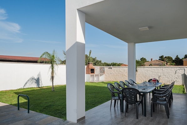 An outdoor patio with a table and chairs, a grill, and a stone wall.