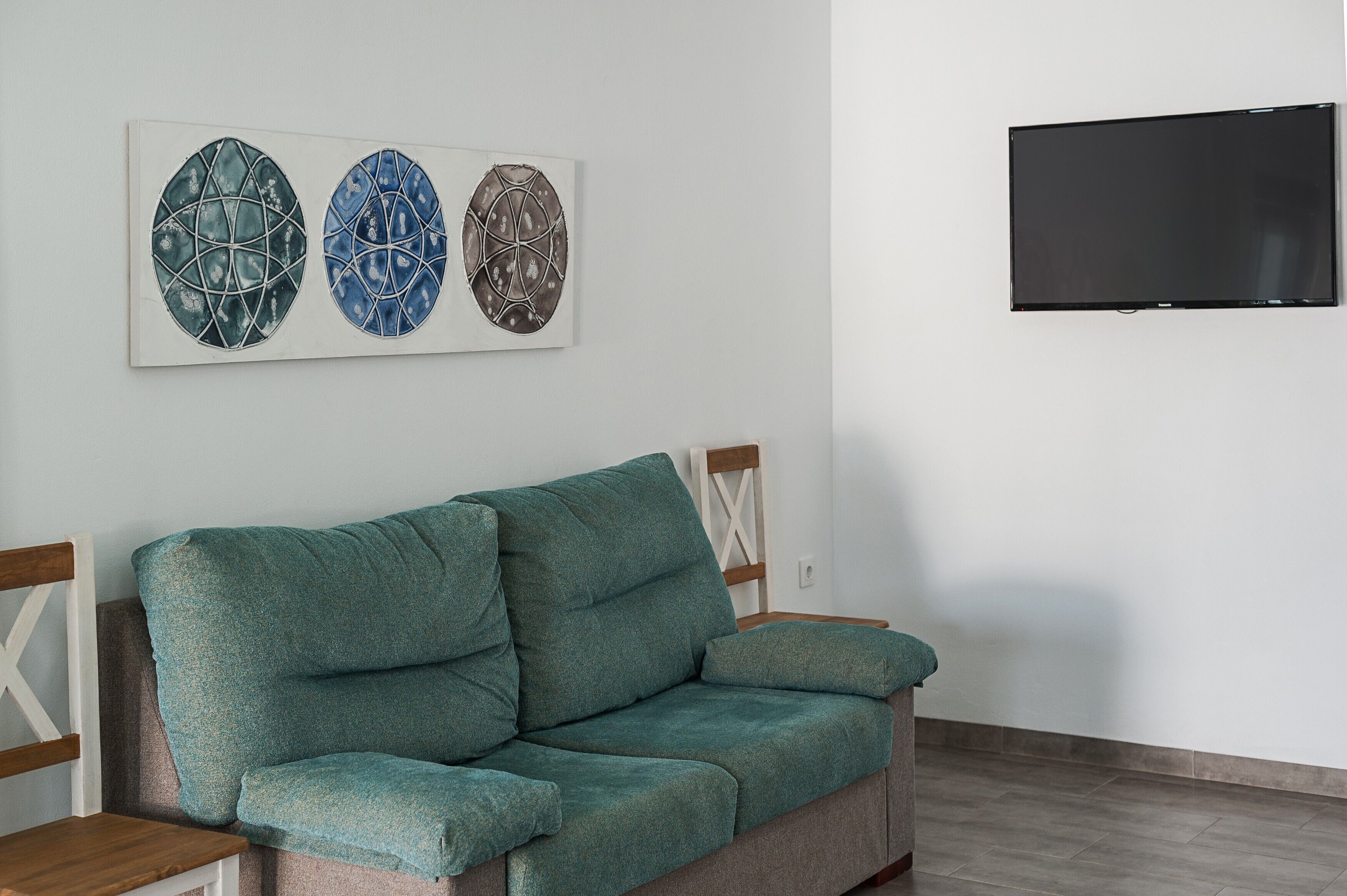 Ein blaugrünes Sofa, eine weiße Wand mit zwei abstrakten Kunstwerken und einem montierten Fernseher.
