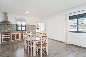 A modern kitchen with a dining area, featuring a tiled backsplash, wooden cabinets, and a large window.