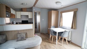 En kompakt opholdsstue med tekøkken, spiseplads og sofa.