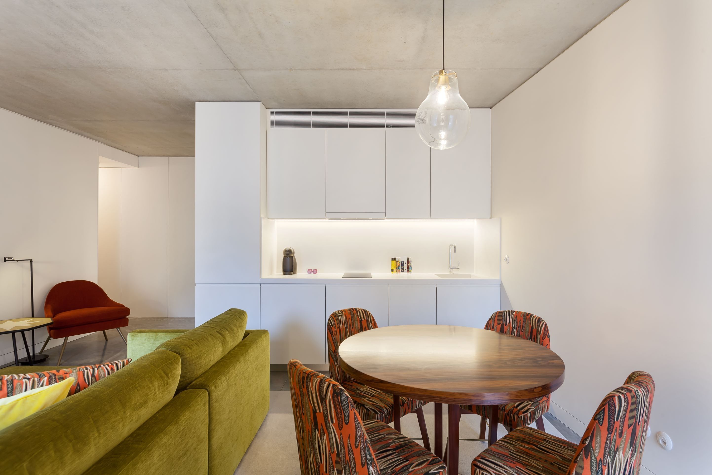 Una cocina moderna con armarios blancos, una mesa de comedor con sillas estampadas, un sofá verde y una silla roja.