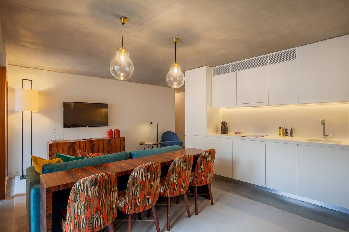 A modern living space with a wooden dining table, colorful patterned chairs, a sofa, and a flat-screen TV.