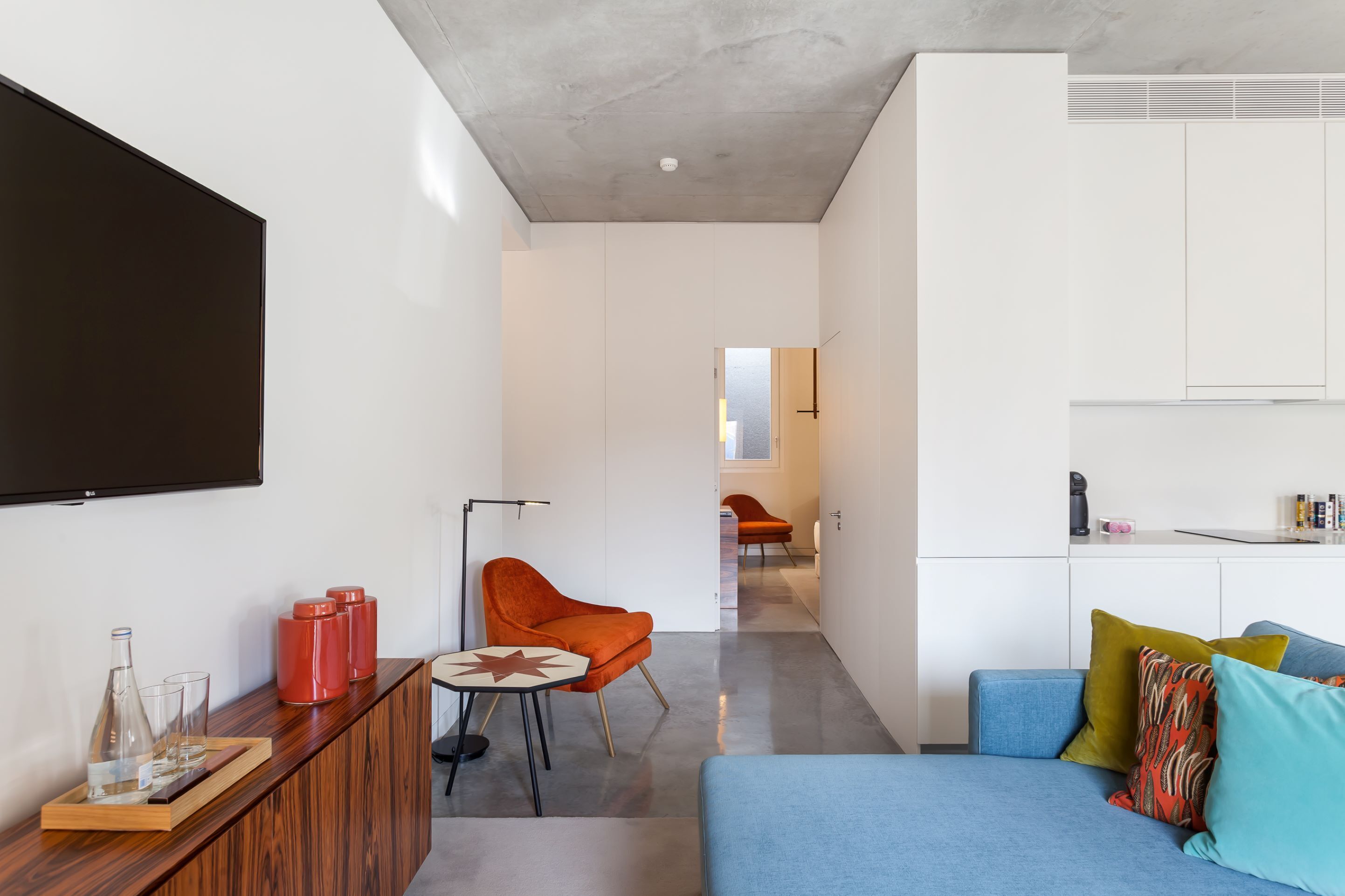 A modern living room with a blue sofa, orange chair, and a wooden side table with glasses and bottles.