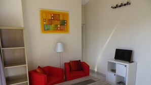 Ett vardagsrum med en röd soffa, ett träbord, en tv-apparat placerad på ett vitt skåp och en bokhylla.