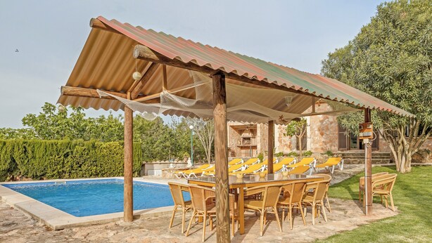 A poolside area with a covered seating area, stone flooring, and a stone building in the background. - Spacious villa with pool – Villa El Bosque (Llucmajor)