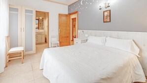 A bedroom with a bed, a nightstand, a chair, a wardrobe, and a bathroom visible through an open door. - Spacious villa with pool – Villa El Bosque (Llucmajor)