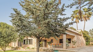 A house with a stone facade, a patio with outdoor furniture, and a large tree in the foreground. - Spacious villa with pool – Villa El Bosque (Llucmajor)