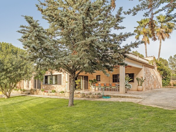 A house with a stone facade, a patio with outdoor furniture, and a large tree in the foreground.