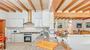A kitchen with white cabinets, a microwave, and a stove. There is a dining area with a white sofa and a table. - Spacious villa with pool – Villa El Bosque (Llucmajor)