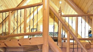Un interior de madera con una escalera, un televisor sobre un mueble de madera y vistas a un baño.