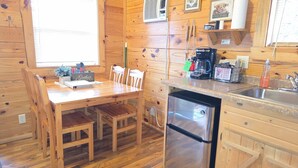 Interior de una cabaña de madera con una mesa de comedor, sillas, un refrigerador, una cafetera y un lavabo.