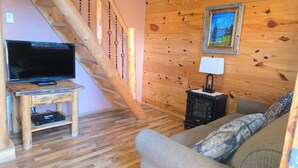 Una sala de estar con escalera de madera, televisor, chimenea y un cuadro en la pared.