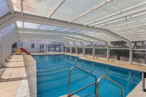 An indoor swimming pool with a glass ceiling, a slide, and a view of the outside. - Spacious Villa "Morena" with Wi-Fi, Garden, Terrace, Balcony & Pool (Albufeira)