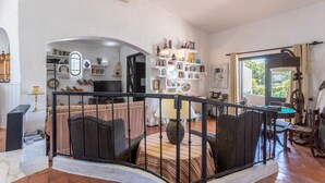 A living room with a sofa, a dining table, a TV, and a bookshelf. - Spacious Villa "Morena" with Wi-Fi, Garden, Terrace, Balcony & Pool (Albufeira)