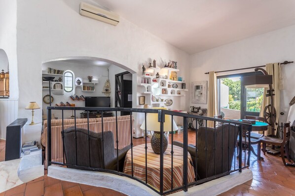 A living room with a sofa, a dining table, a TV, and a bookshelf. - Spacious Villa "Morena" with Wi-Fi, Garden, Terrace, Balcony & Pool (Albufeira)
