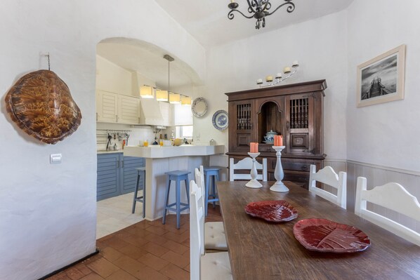 A kitchen with a central island, white bar stools, a wooden dining table, and a chandelier.