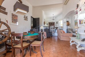 A spacious living area with a wooden dining table, chairs, a sofa, and a patterned floor.