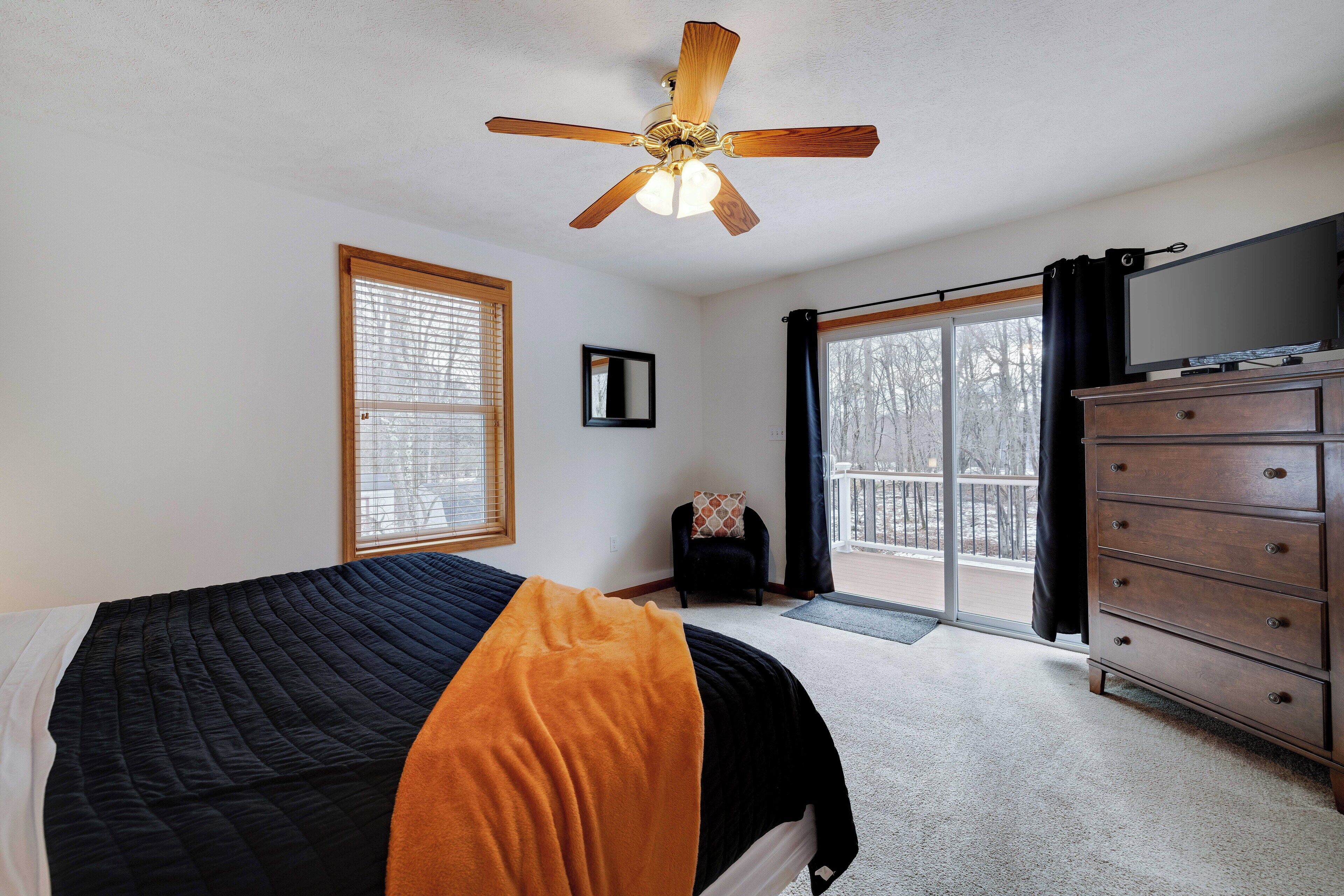A bedroom with a bed, a wooden dresser, a television, and a ceiling fan.