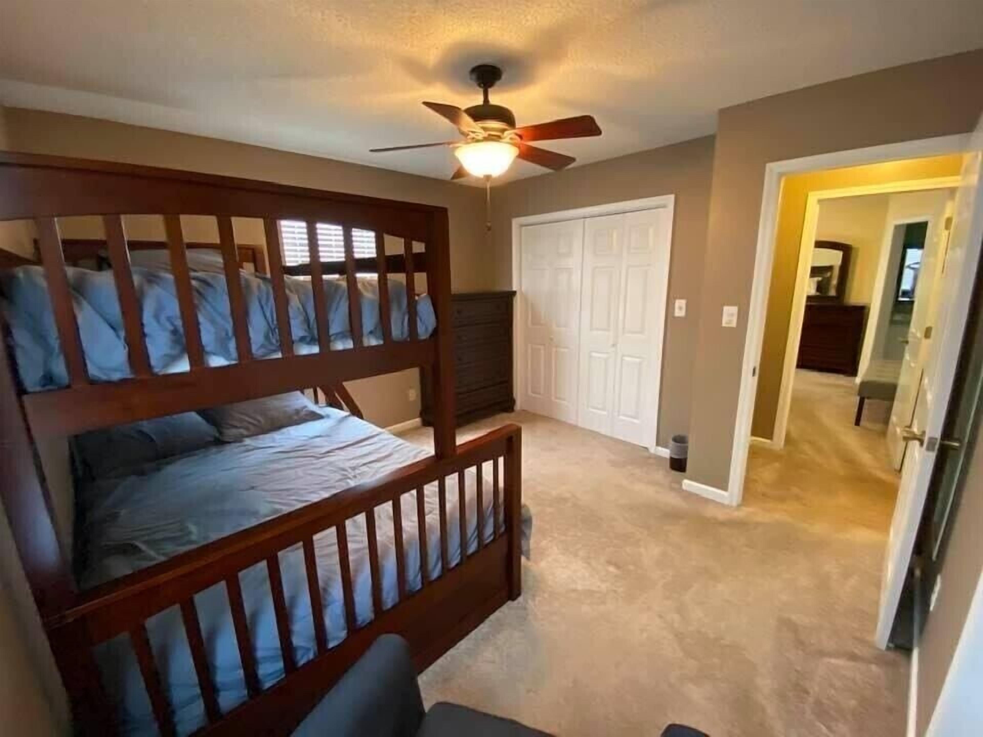 Une chambre avec un lit superposé, un ventilateur de plafond, une porte et un sol recouvert de moquette.