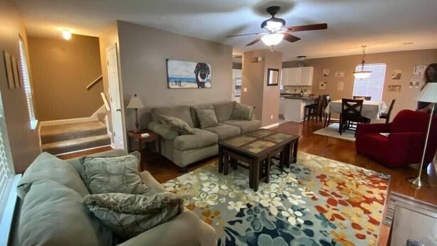 Ein Wohnzimmer mit einer Couch, einem Couchtisch und einem gemusterten Teppich. Eine Treppe führt zu einer weiteren Ebene.