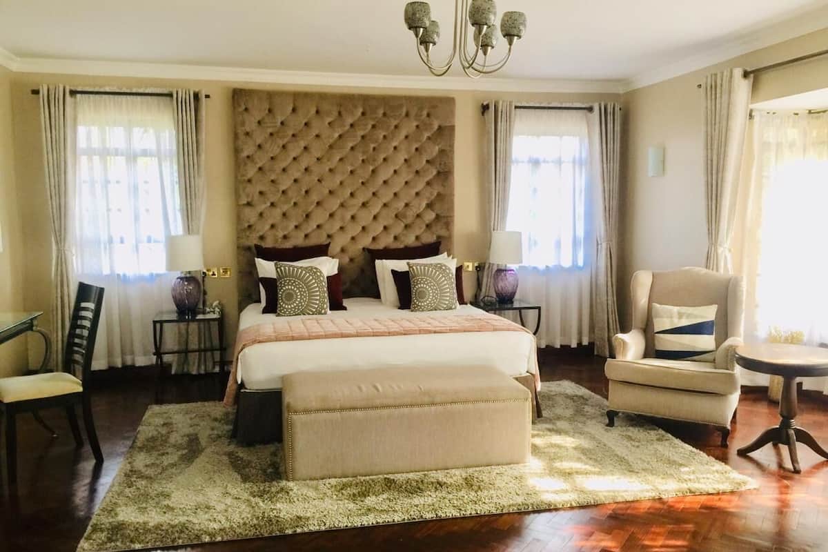 Une chambre spacieuse avec un grand lit, une tête de lit capitonnée, une chaise longue et une table ronde.