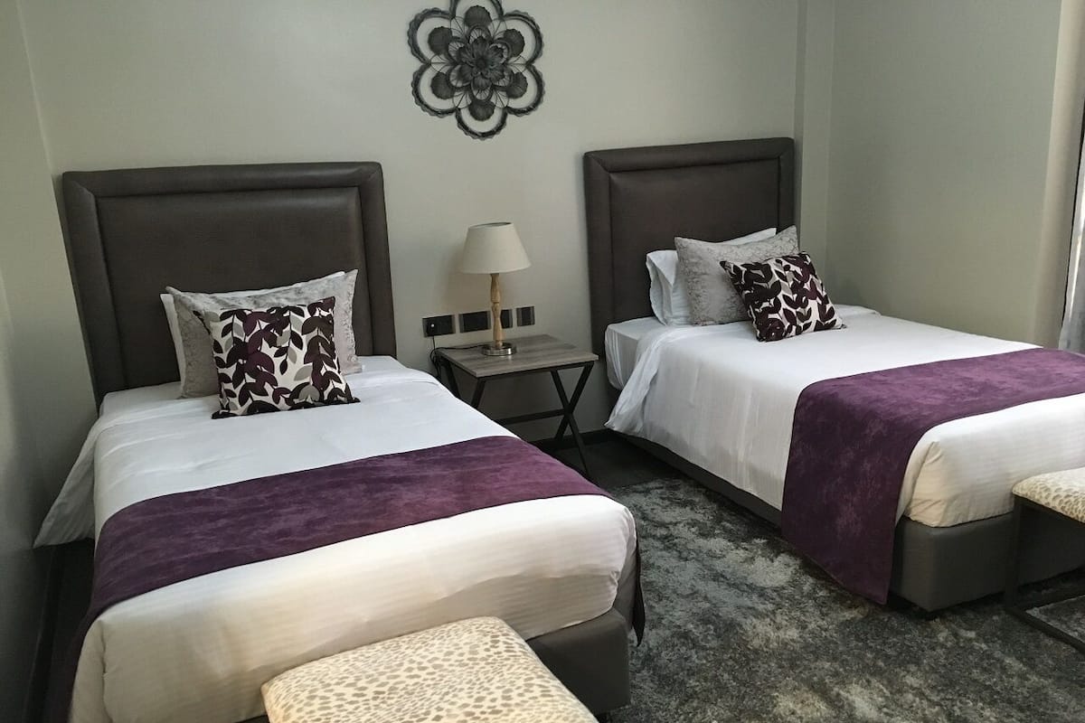 Une chambre d’hôtel avec deux lits, chacun doté d’une tête de lit, d’une table de chevet avec une lampe et d’un élément décoratif mural.