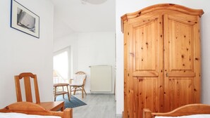 A bedroom with two wooden beds, a wooden wardrobe, a wicker chair, a small table, and a radiator.