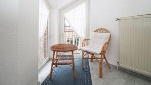 A narrow hallway with a wicker chair and a small round table, white curtains, and a radiator.