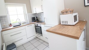 A compact kitchen with white cabinets, a wooden countertop, a microwave, and a coffee maker.