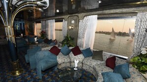 Un coin salon accueillant avec des canapés et une table basse en verre, de grandes fenêtres avec des rideaux et une vue sur les bateaux sur l’eau.