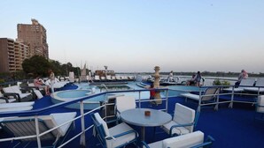 Un espace piscine aménagé sur le toit, avec des chaises longues et des tables, entouré d’une terrasse bleue et offrant une vue sur le panorama urbain.