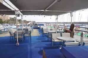 A covered outdoor seating area with tables and chairs, overlooking a marina with boats. - Diamond ship Hotel (Cairo)