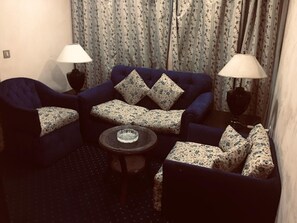 A room with a dark blue sofa set, two matching armchairs, a small round coffee table, and two floor lamps. - Diamond ship Hotel (Cairo)