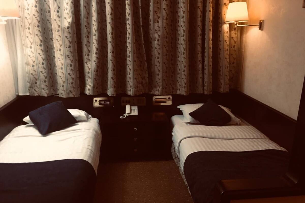 A hotel room with two beds, a bedside table with a lamp, and a telephone.