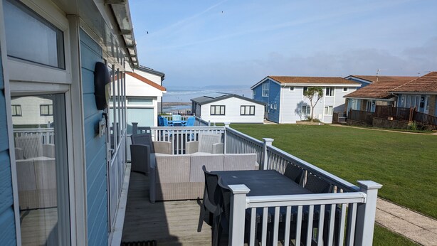 A deck with outdoor furniture, a view of the ocean, and a row of beach houses. - 2-bedroom sea view property 1 min from the sea & SW Coast Path (Bideford)
