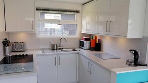 A modern kitchen with white cabinets, a built-in microwave, a kettle, and a toaster. - 2-bedroom sea view property 1 min from the sea & SW Coast Path (Bideford)