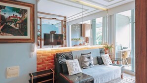A modern living room with a leather sofa, a TV, and a kitchen area visible through a glass partition.
