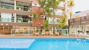 A modern hotel with a swimming pool, outdoor seating, and palm trees.