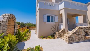 Una casa moderna de dos pisos con entrada de piedra, un porche cubierto y un jardín bien cuidado.