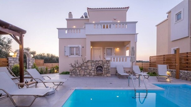Un edificio de dos plantas con piscina, mobiliario exterior y chimenea de piedra.