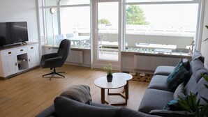 Een moderne woonkamer met een bank, een salontafel, een televisie en een eethoek met een tafel en stoelen.