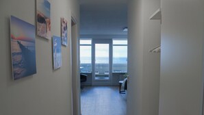 Een gang met uitzicht op de oceaan door grote ramen, een stoel en enkele ingelijste foto’s aan de muur.