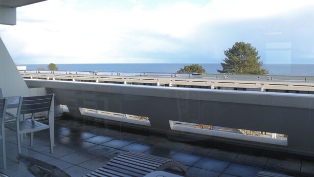 Een balkon met uitzicht op zee, een leuning en een bank.