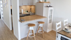 Een moderne keuken met een houten aanrecht, twee krukken, een spoelbak en een eettafel met stoelen.
