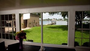 Blick aus einem Zimmer mit großen Fenstern auf einen grünen Rasen und einen Steg, der sich in einen See erstreckt.