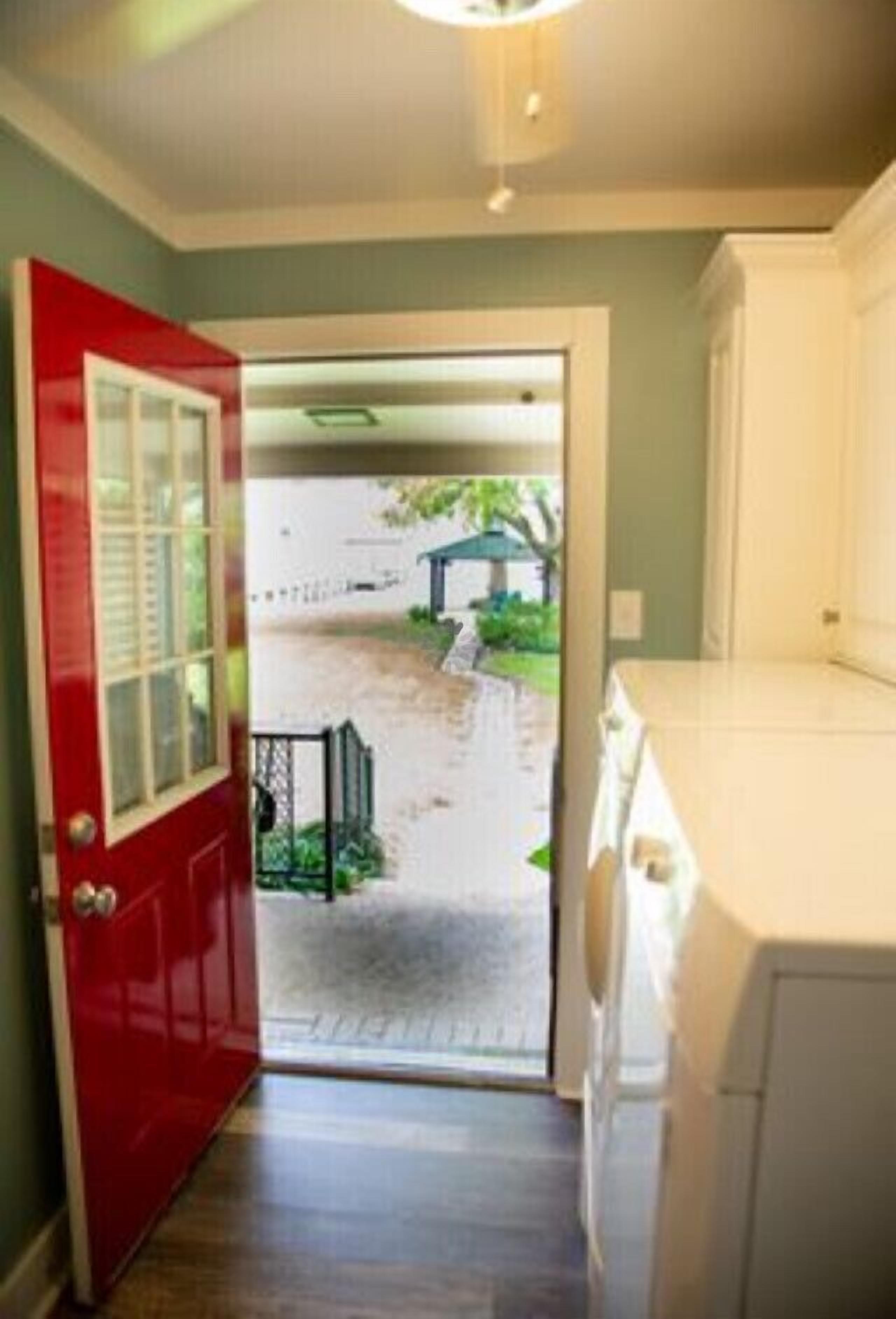 Una habitación con una puerta roja, un armario blanco y vistas de un jardín a través de la puerta.