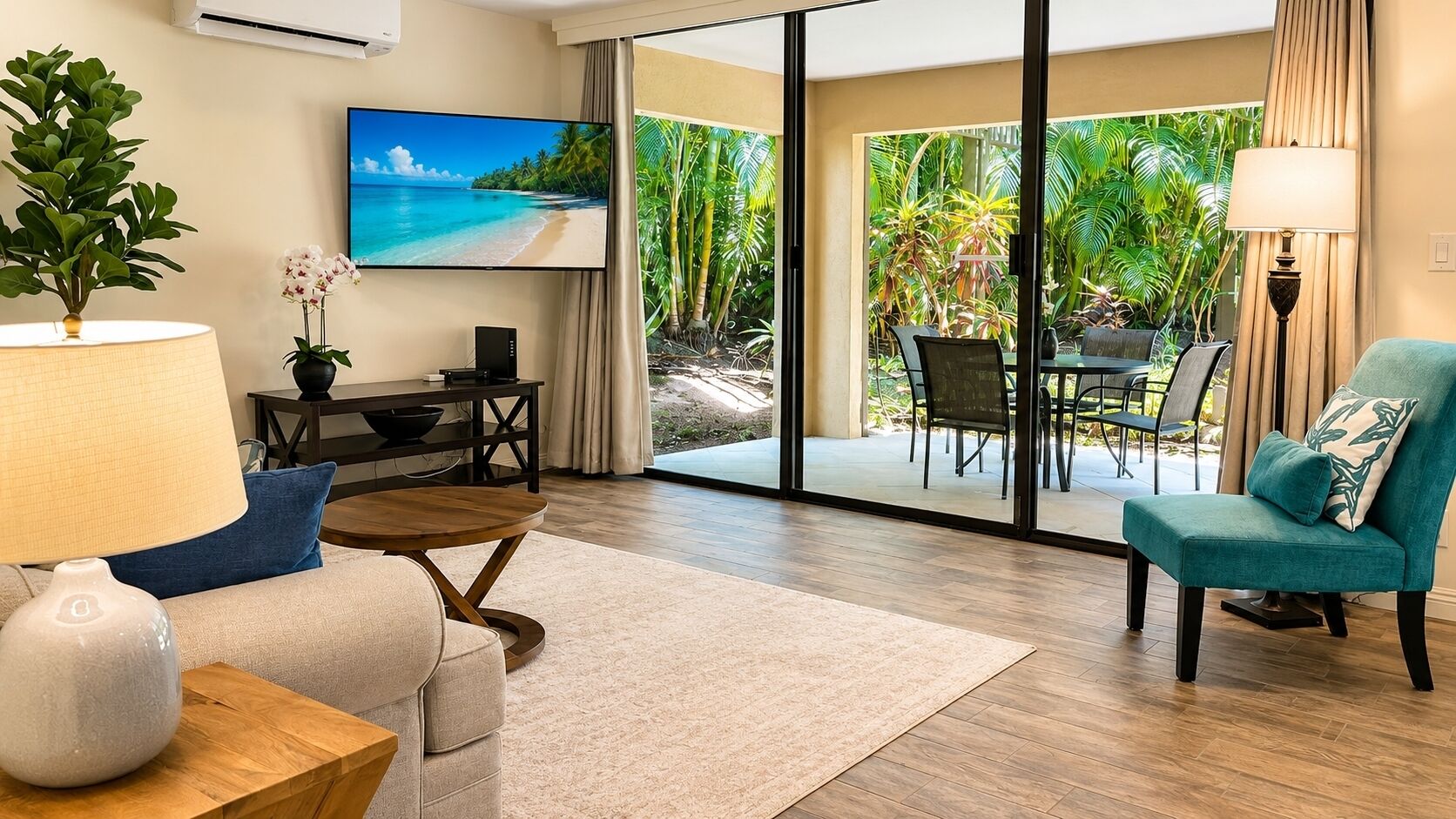 Una sala moderna con un sofá, una mesa de centro y un sillón verde azulado. Un televisor de pantalla plana está montado en la pared, y se ve un jardín tropical a través de las puertas de cristal.