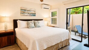 A bedroom with a bed, bedside tables, a window with blinds, and a view of the outside. - Lush Wailea Ground Floor Condo Tropical Oasis Four Pools Keawakapu Beach (Wailea)