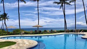 A pool with lounge chairs and umbrellas, surrounded by palm trees and a view of the ocean. - Lush Wailea Ground Floor Condo Tropical Oasis Four Pools Keawakapu Beach (Wailea)
