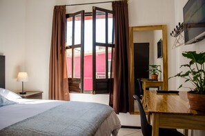 Una habitación de hotel con cama, escritorio, silla, lámpara, televisor y planta en maceta.